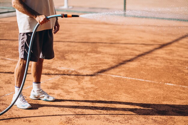 Hombre regando cancha de tenis antes del partido