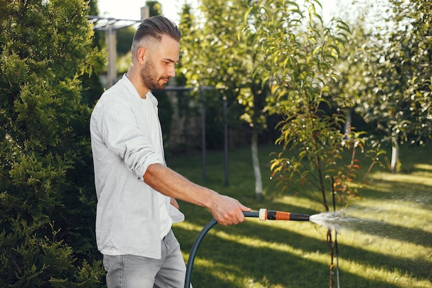 Hombre regando sus plantas en su jardín. Hombre con camisa azul.