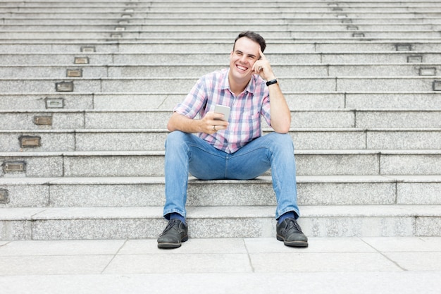 Hombre relajado que usa Smartphone en la escalera de la ciudad