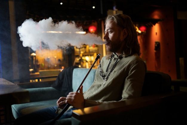 Hombre relajándose vaping de una pipa de agua en un bar.