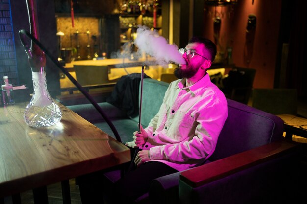 Hombre relajándose vaping de una pipa de agua en un bar.