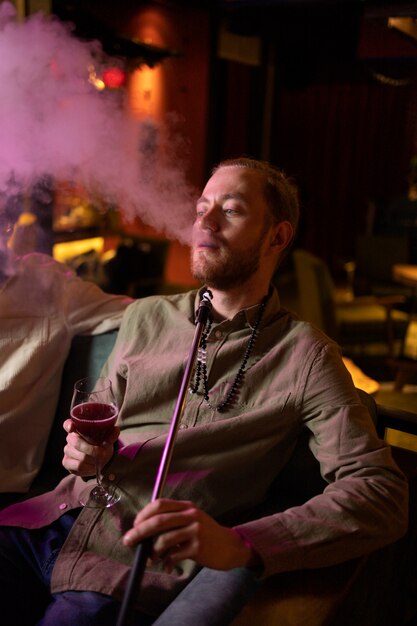 Hombre relajándose vaping de una pipa de agua en un bar.