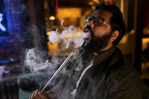 Hombre relajándose vaping de una pipa de agua en un bar.