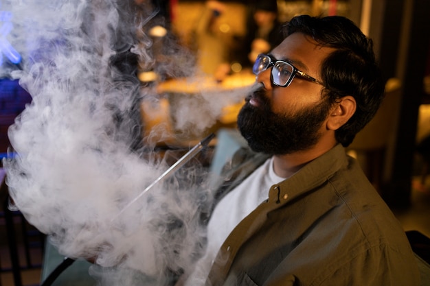 Hombre relajándose vaping de una pipa de agua en un bar.