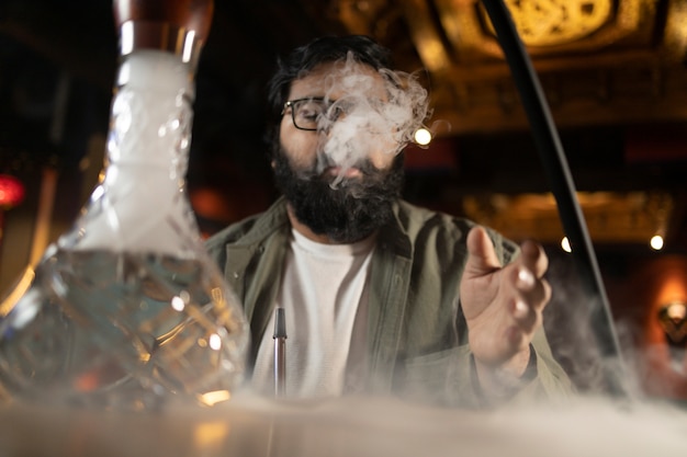 Hombre relajándose vaping de una pipa de agua en un bar.