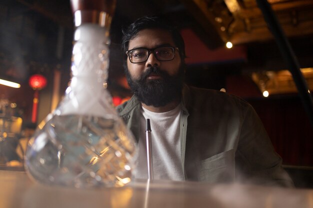 Hombre relajándose vaping de una pipa de agua en un bar.