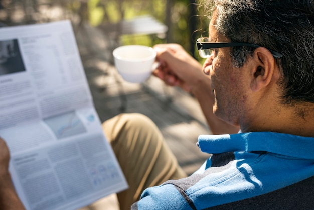 Foto gratuita hombre relajante mientras lee un periódico y toma café