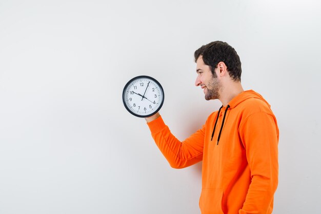 El hombre del reloj de pared que sostiene está mirando a la izquierda sobre fondo blanco.