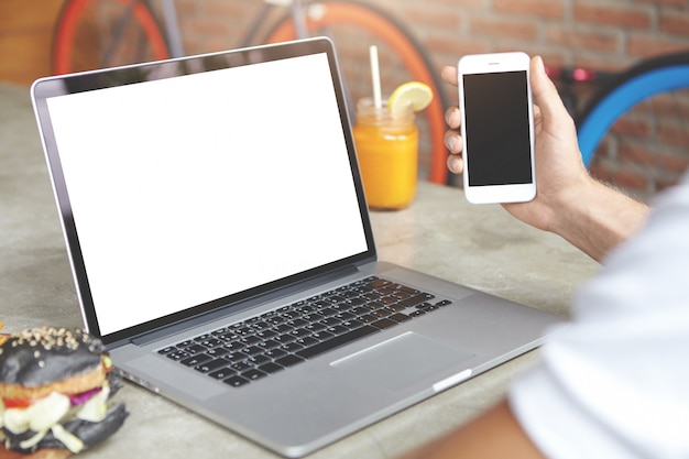 Hombre revisando el correo electrónico, utilizando una conexión a Internet de alta velocidad en dispositivos electrónicos. Hombre con teléfono inteligente en la mano, sentado frente a la computadora portátil abierta