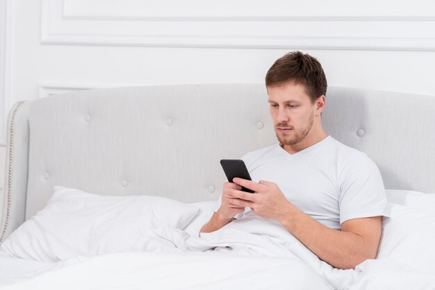 Hombre revisando su teléfono después de despertarse con espacio de copia