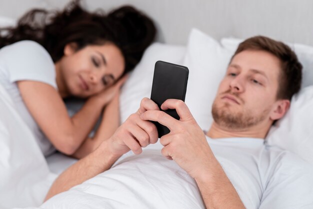 Hombre revisando su teléfono junto a la novia dormida