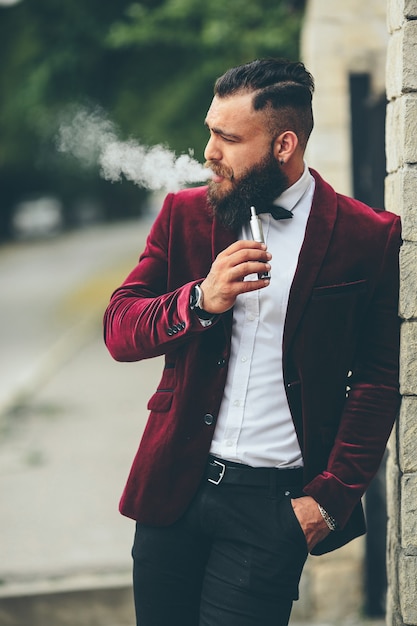 Hombre rico con barba fuma cigarrillo electrónico