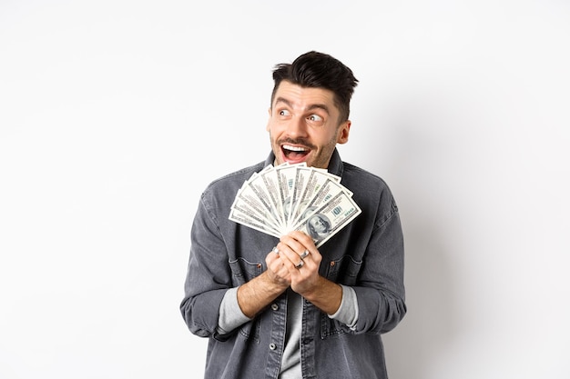 Un hombre rico y feliz soñando con comprar billetes de un dólar en las manos mirando a un lado pensativo y sosteniendo dinero contra el fondo blanco