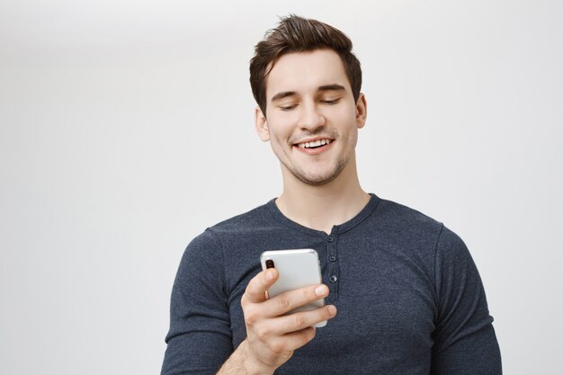Hombre riendo complacido mirando la pantalla del teléfono móvil y sonriendo