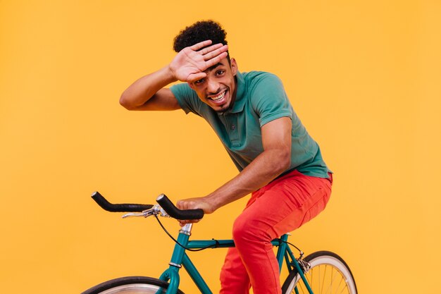 Hombre riendo con peinado rizado sentado en bicicleta. chico africano en traje colorido montando en bicicleta.