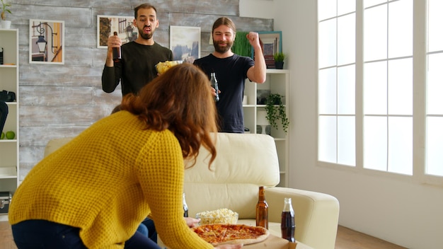 Foto gratuita hombre riéndose y alcanzando una porción de pizza mientras ve televisión con sus amigos. reunión de amigos cercanos.