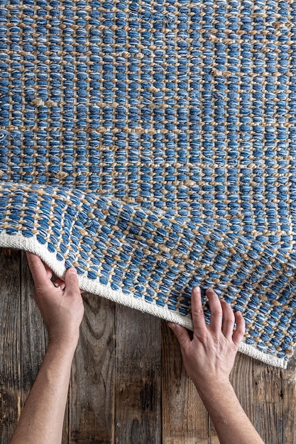 Foto gratuita hombre rodando una alfombra de denim geométrica tejida a mano en un piso de madera en casa