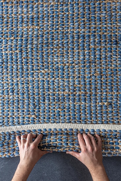 Foto gratuita hombre rodando una alfombra de denim geométrica tejida a mano en un piso de madera en casa