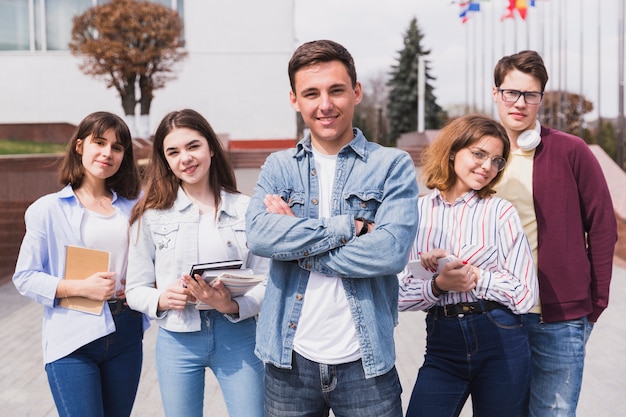 Hombre rodeado de estudiantes inteligentes con libros mirando a cámara