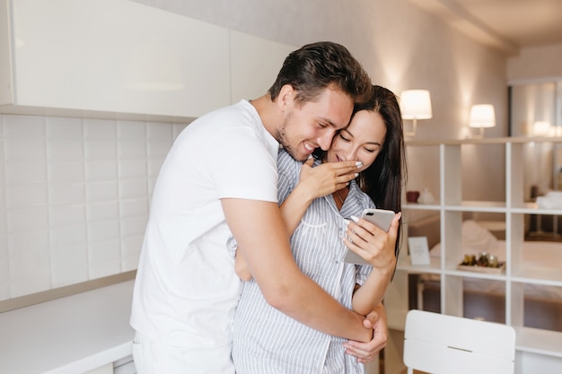 Hombre romántico con peinado corto abrazando a una dama morena riendo viste un pijama lindo