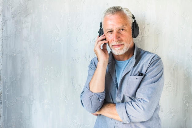 Hombre en ropa casual escuchando música en auriculares de pie contra la pared de hormigón