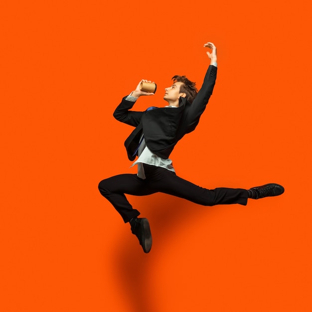 Hombre en ropa casual de estilo de oficina saltando y bailando aislado en naranja brillante