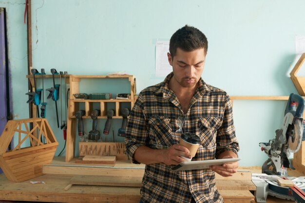 Hombre en ropa casual revisando correos electrónicos con carpintería en el fondo