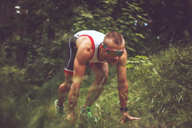 Hombre con ropa deportiva y gafas de sol corriendo por el bosque.