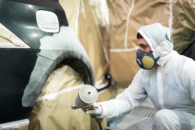 Hombre con ropa protectora y máscara de pintura parachoques de automóvil en taller de reparación