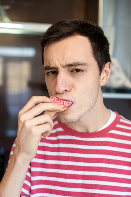 Un hombre con rostro serio comiendo una rosquilla en la cocina