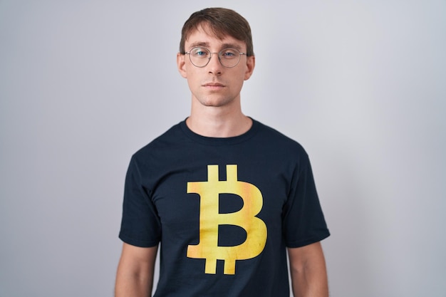 Hombre rubio caucásico con camiseta de bitcoin escéptico y nervioso, frunciendo el ceño molesto por el problema. persona negativa