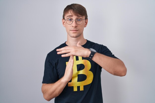 Hombre rubio caucásico con camiseta de bitcoin haciendo gesto de tiempo fuera con las manos, cara frustrada y seria