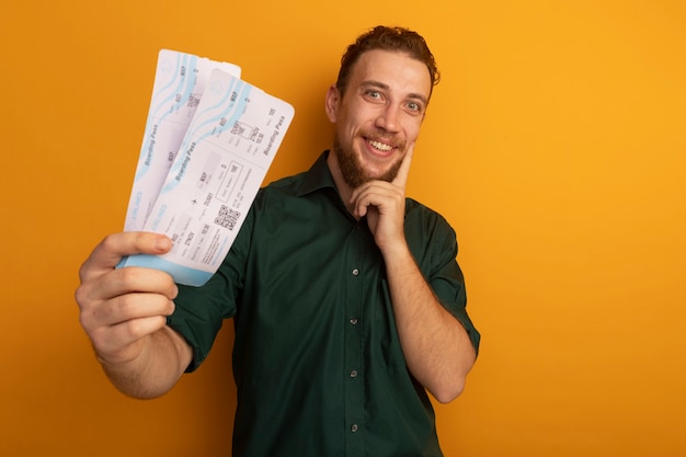 Foto gratuita hombre rubio guapo emocionado sostiene boletos de avión y pone el dedo en la cara aislada en la pared naranja