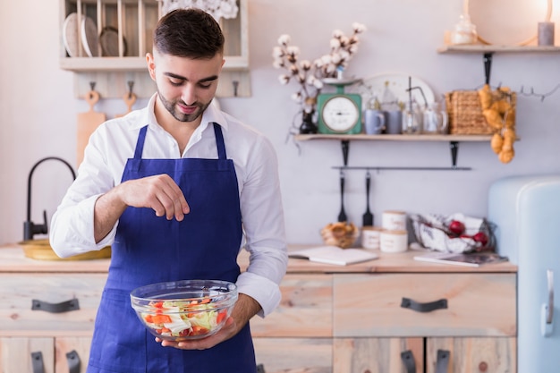 Hombre salado ensalada en un tazón en la cocina