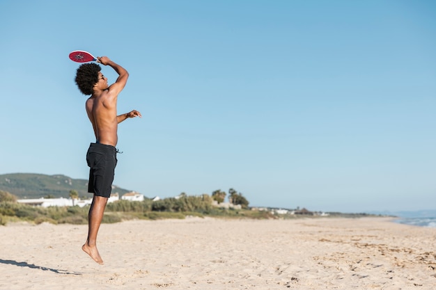 Hombre saltando con raqueta de tenis en la playa