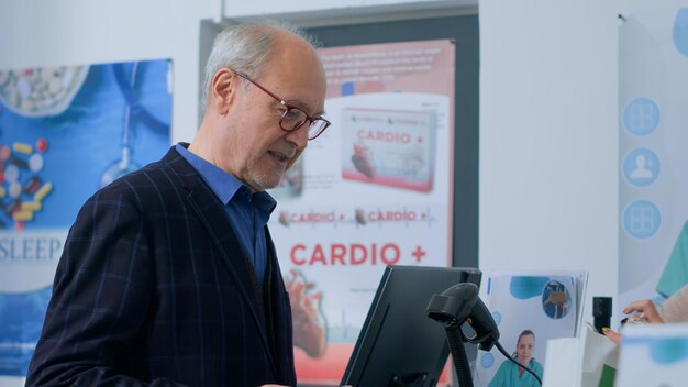 Un hombre senescente llega al mostrador de la farmacia después de encontrar los artículos médicos necesarios, compra píldoras para la prevención de enfermedades con tarjeta de crédito y recibe ayuda de un farmacéutico con una bolsa de compras.