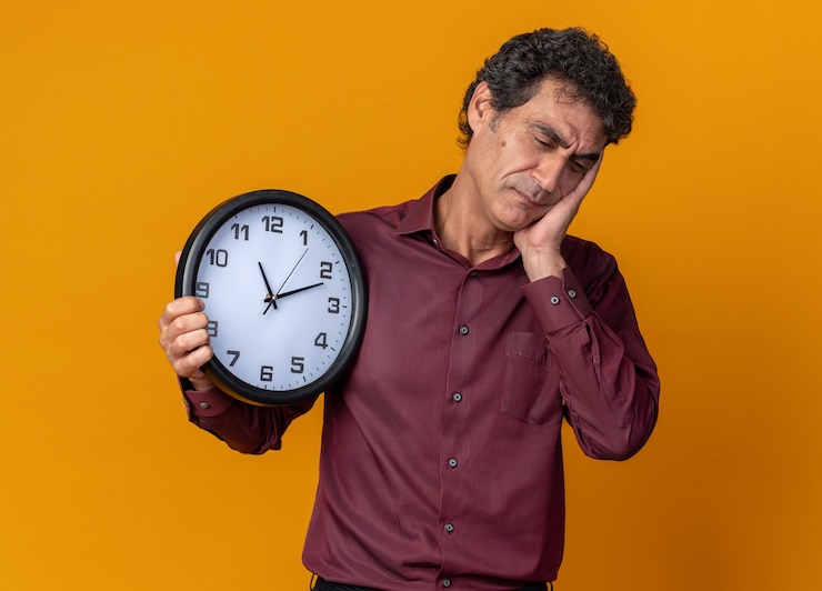 Foto gratuito hombre senior en camisa púrpura con reloj de pared con aspecto cansado y aburrido