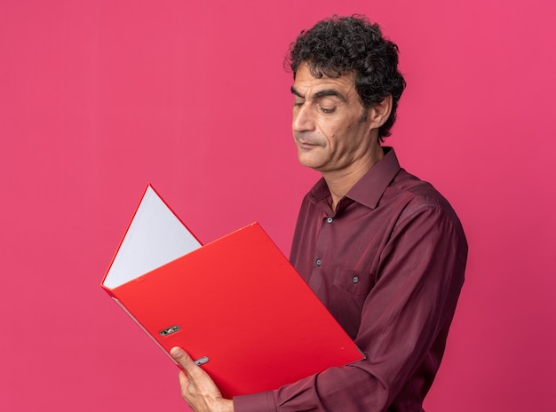 Hombre senior en camisa púrpura sosteniendo la carpeta abierta mirándolo con cara seria