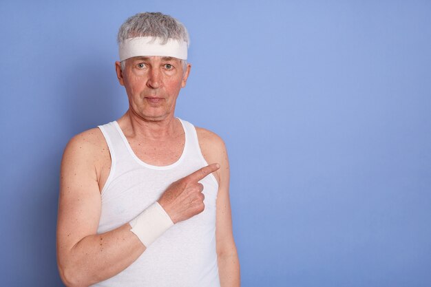 Foto gratuita hombre senior en camiseta blanca mirando y apuntando a un lado con su dedo índice