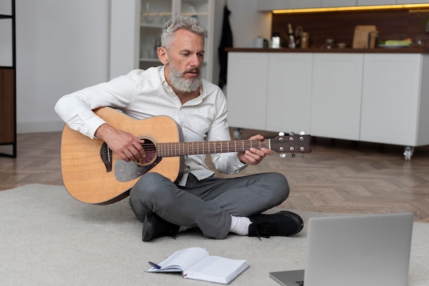 Foto gratuita hombre senior en casa en el piso tomando lecciones de guitarra