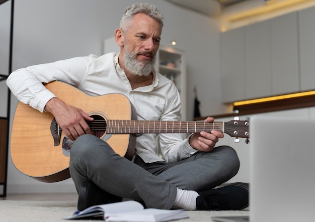 Foto gratuita hombre senior en casa en el piso tomando lecciones de guitarra