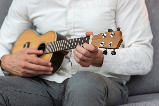 Hombre senior en casa tocando el ukelele en el sofá