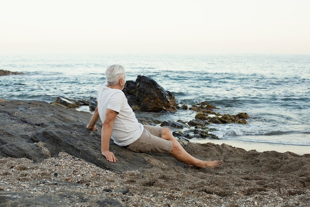 Hombre senior descansando en la playa y admirando el océano