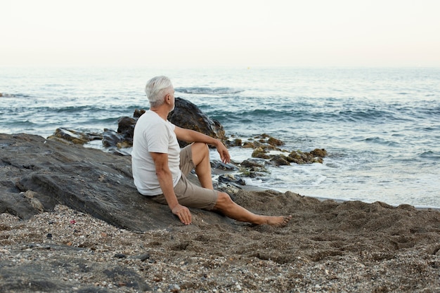 Hombre senior descansando en la playa y admirando el océano