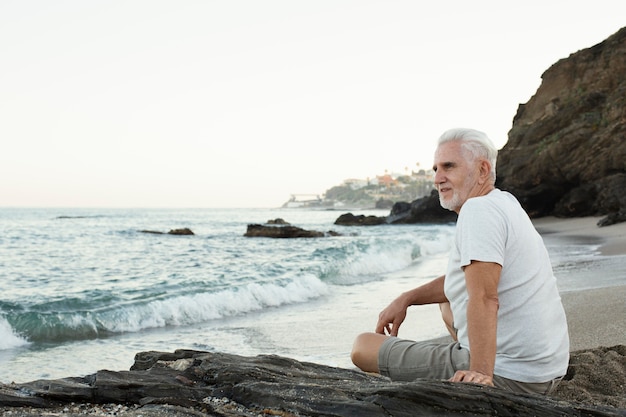 Hombre senior descansando en la playa y admirando el océano