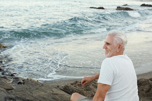 Hombre senior descansando en la playa y admirando el océano