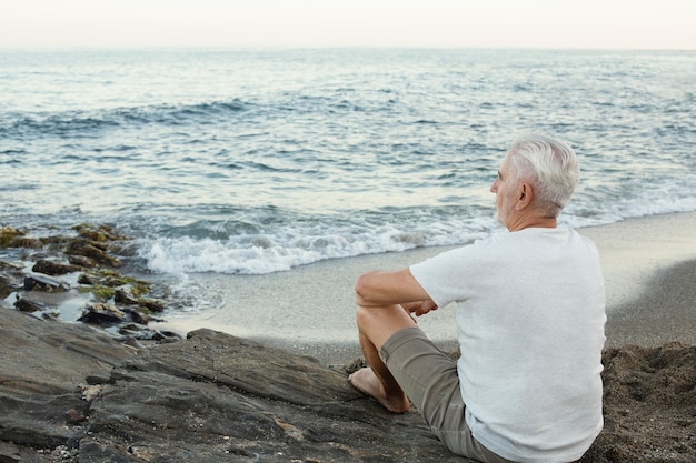 Hombre senior descansando en la playa y admirando el océano