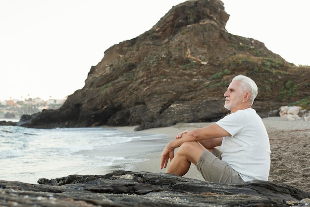 Hombre senior descansando en la playa y admirando el océano