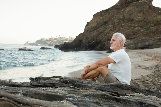 Hombre senior descansando en la playa y admirando el océano