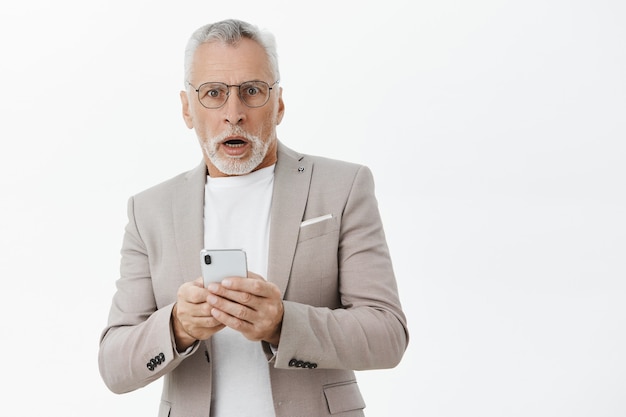 Hombre senior jadeando sorprendido mirando, con smartphone